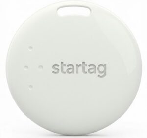 A round, white electronic tag with the word startag embossed in the center. The tag has a small slot at the top and three small dots on the left side. The background is plain white with black borders.