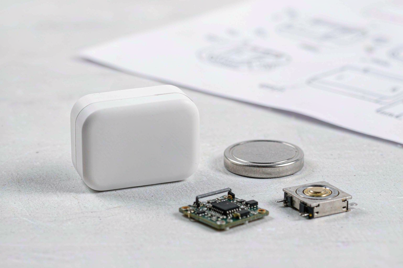 Unbranded Bluetooth tracker, coin-cell battery, circuit board and acoustic transducer on an engineering workbench
