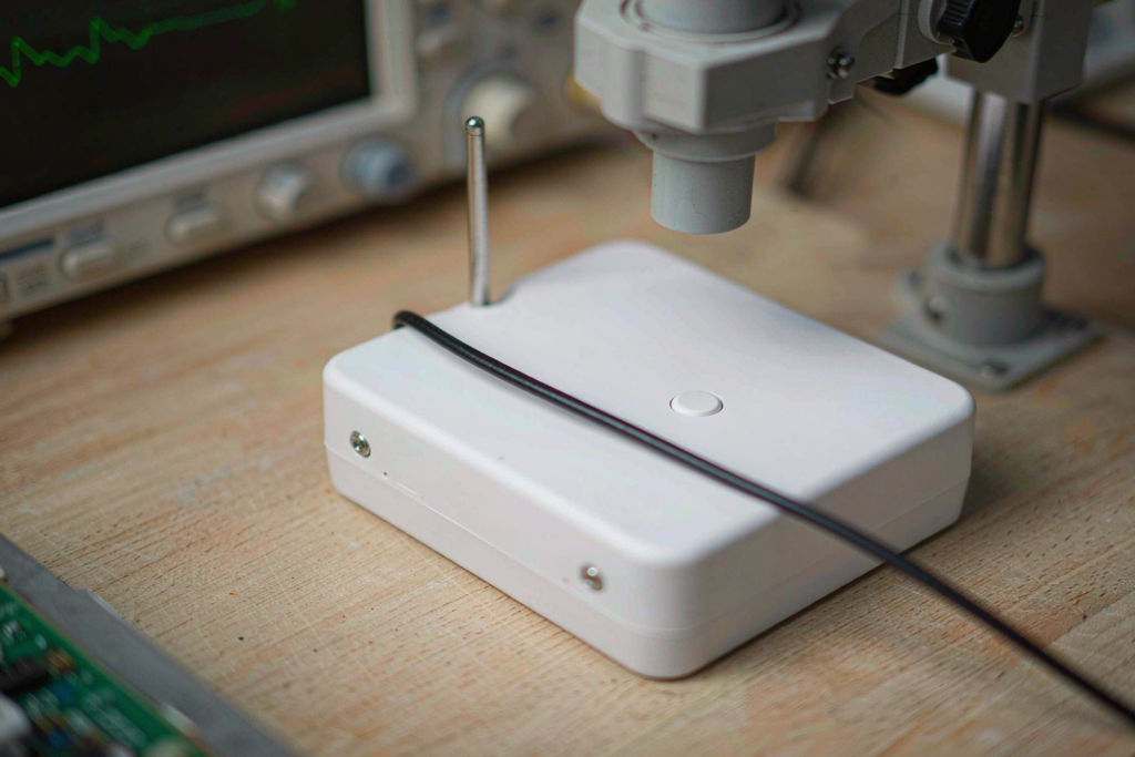 Unbranded Bluetooth tracker prototype on an electronics engineering workbench with measurement equipment